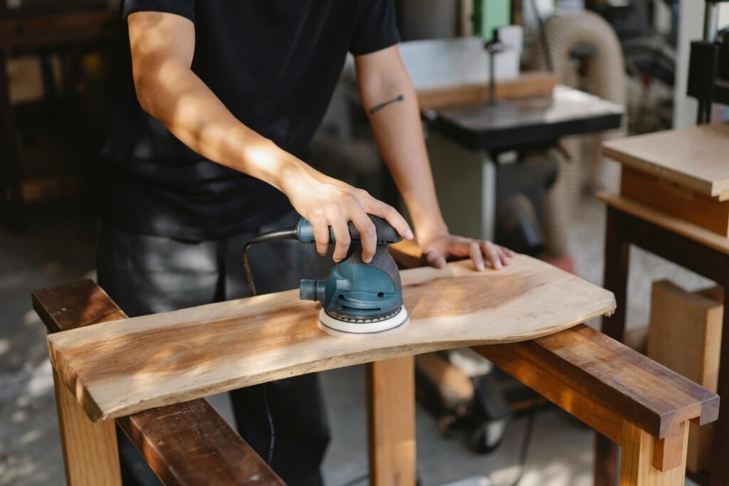 pexels-photo-5974325-5974325 A craftsman uses a power sander on a wooden plank in a well-lit workshop.